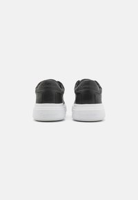 Black sneakers with a smooth leather upper, white rubber sole, and embossed logo on the back. Rounded shape with padded collar.