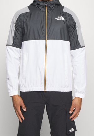 Mann trägt eine schwarze, graue und weiße The North Face Zip-up Jacke und schwarze Cargo-Shorts mit dem The North Face Logo.