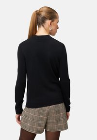 Schwarzer Strickpullover mit langen Ärmeln und rundem Ausschnitt, kombiniert mit beigen karrierten Shorts. Glatte Textur und figurbetontes Design.