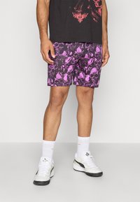 Lilla og sorte shorts med et kraniummønster, lavet af letvægtsstof, parret med hvide sneakers og ankelsokker. Casual stil.