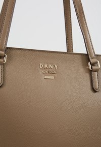 Sac à main DKNY en cuir marron texturé avec logo doré et double bretelles, sur fond blanc.