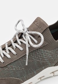 Šedé textilní tenisky s pleteným designem, semišovými akcenty a bílými tkaničkami. Obsahují logo na patě a zdrsněnou gumovou podrážku.