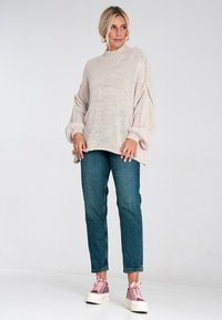 Jasno beżowy sweter z dzianiny z wysoką szyją i luźnymi rękawami, zestawiony z niebieskimi dżinsami i różowymi sneakersami na platformie.