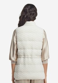 Vitt quiltat väst med fiskbensmönster, hög krage och figursydd stil. Texturen är mjuk och kompletteras av en glansig beige topp.