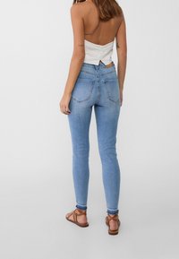 Vaqueros ajustados de color azul con una cintura alta, que presentan una textura de denim suave y dos bolsillos traseros, estilizados con un ligero desgaste y detalles de costura.