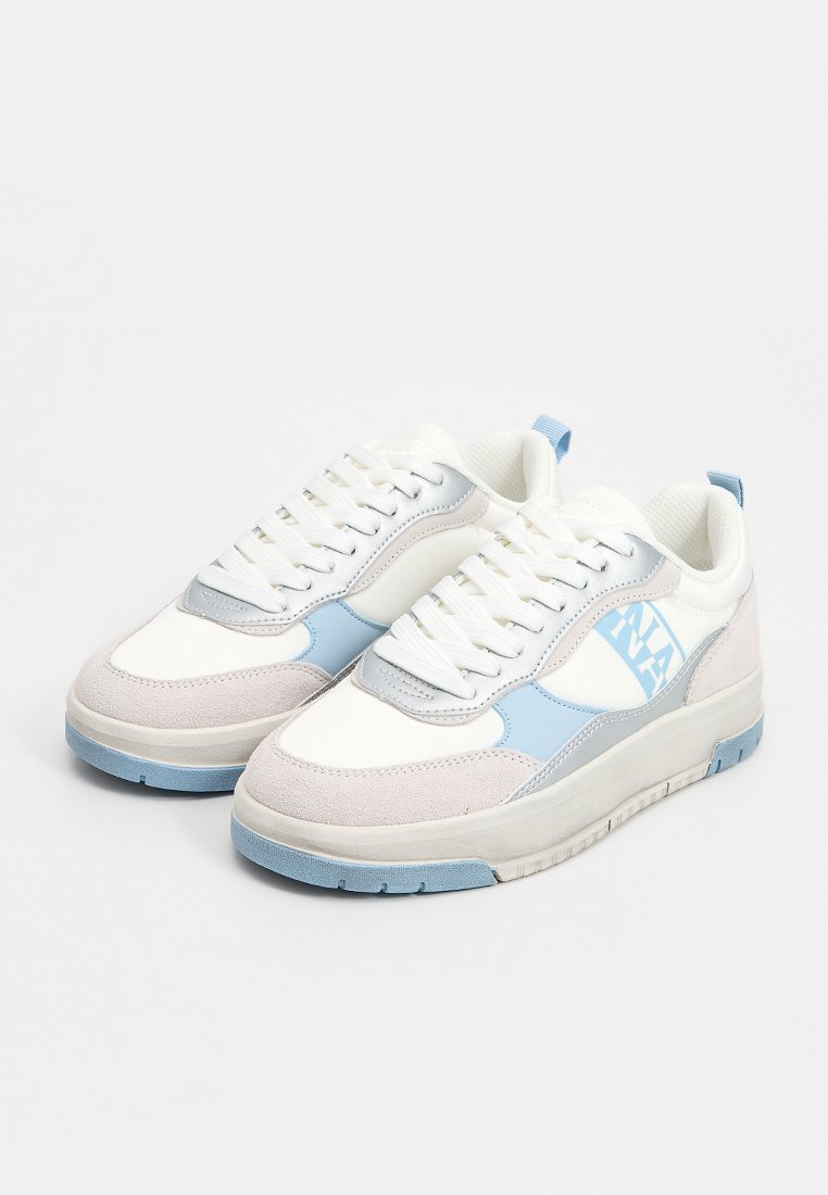 Zapatillas blancas con detalles en azul claro y gris. Materiales de cuero liso y ante. Presentan una suela de goma texturizada y un diseño con cordones.