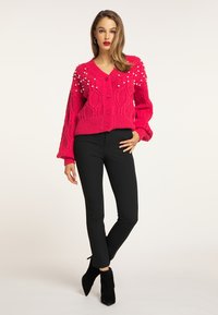 Cardigan tricotat roz cu model în cablu, embellisări cu perle la umeri și închidere cu butoane, asortat cu pantaloni negri mulați și cizme ankle.