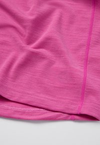 Lähedalt vaadatuna erksaroosa kangas, millel on nähtavad kumerad õmblused ja pehmed voldid tasasel pinnal.