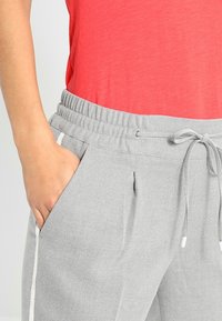 Jogging gris à motifs avec une taille élastique et un cordon de serrage, dotés de poches latérales et d'accents latéraux blancs contrastants.