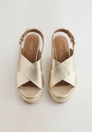 Sandali platform in pelle dorata con cinturini incrociati, design slingback e suola in stile espadrilles intrecciata. Presentano una chiusura laterale con fibbia.