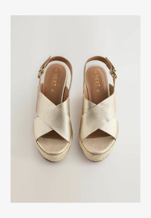 Złote skórzane sandały na platformie z krzyżującymi się paskami, z designem slingback oraz plecioną podeszwą w stylu espadryli. Posiadają zapięcie na klamrę z boku.