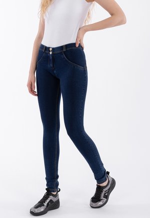 Jeans skinny en denim bleu foncé avec une texture lisse, présentant une fermeture à double bouton, des poches frontales et des coutures contrastées.