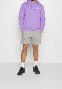 Lila hoodie med framficka och logotyp, kombinerad med grå shorts och svarta sneakers. Vita strumpor med logotypdetaljer.