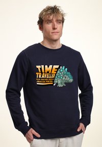 Felpa blu navy con un design grafico che presenta un dinosauro in stile cartone animato e il testo "VIAGGIATORE DEL TEMPO DA UN ALTRO MONDO PORTALE GIURASSICO."
