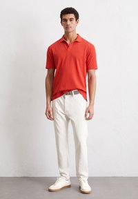 Rode polo met korte mouwen en een kraag, gecombineerd met off-white broeken en witte sneakers met tan zool.