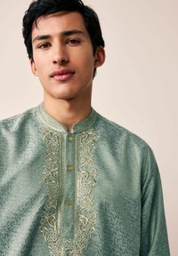 Zöld hímzett kurta mandarin gallérral, virágmintákkal, arany díszítésekkel és öt aranygombbal a gombolás mentén.
