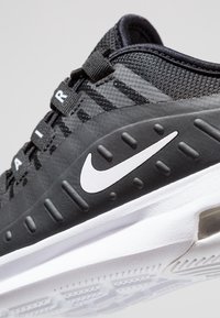 Zapatilla deportiva negra con parte superior texturizada, logo blanco y suela acolchada. Presenta cordones y una unidad de aire prominente para mayor soporte.