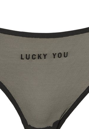 Svart bikinitrosa i meshtyg med låg midja. Texten "LUCKY YOU" i fet stil i svart på framsidan. Slät textur, minimalistiska kanter.