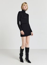 Schwarzes langärmliges Turtleneck-Oberteil mit passgenauer Silhouette, kombiniert mit einem schwarzen Minirock und kniehohen schwarzen, glänzenden Stiefeln mit spitzen Zehen.