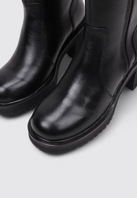 Black leather ankle boots with a smooth finish, rounded toe, and block heel. Features side zipper and textured rubber sole for grip.