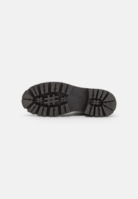 Black rubber shoe sole with a textured tread pattern. Features deep grooves and various shaped lugs for traction. Flat construction style.