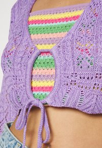 Top cropped de malha roxa com um centro aberto e fecho de laço, sobreposto a um top de alças riscado multicolorido. Detalhes de padrão texturizado.