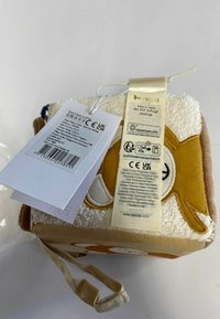 Fabric cube plush toy featuring a soft brown, yellow, and white design with animal face, loop handle, and attached care labels.