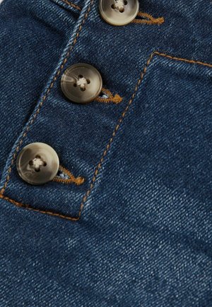 Denim audums vidēji zilā tonī, ar trim apaļām, caurspīdīgām pogām un pretējo apelsīnu diedzi gar šuvi.