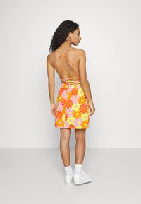 Vestido colorido com um padrão floral em laranja, rosa e amarelo. Apresenta alças cruzadas finas e uma silhueta ajustada com um detalhe de laço.