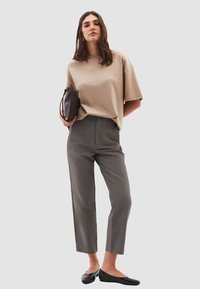 Camiseta beige de gran tamaño con hombros caídos, pantalones de rayas grises y bailarinas negras. La modelo lleva un pequeño bolso marrón.