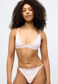 Set roz de sutien și tanga cu modele de inimă, dantelă la margini și bretele reglabile. Materialul are o textură netedă.