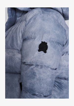 Pehmead sinihallid jope tekstureeritud viimistlusega, millel on ümar must logo plekk varrukal ja kapuuts.