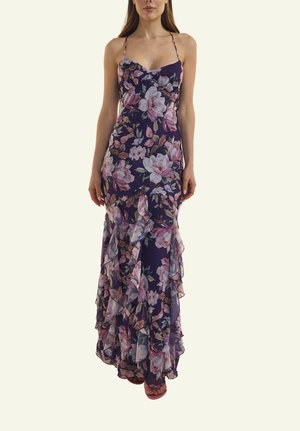 Frau trägt ein bodenlanges, ärmelloses, violettes Blumenkleid mit Rüschendetails und dünnen Schulterträgern.