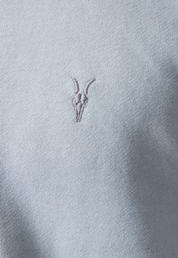 Maglione azzurro chiaro con lavorazione a maglia texture e un piccolo ricamo pallido di teschio di capra sul petto.