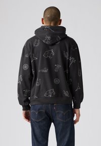 Donkergrijze hoodie met witte omtrekgraphics, waaronder dieren en voorwerpen. Bevat een capuchon en een kanga pocket. Gecombineerd met donkere jeans.