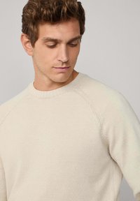 Hellbeige gestrickter Pullover mit einem gerippten Kragen und strukturierten Akzenten. Verfügt über einen klassischen Rundhalsausschnitt und Raglanärmel.