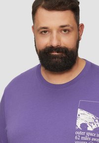 Purple short-sleeve t-shirt made of cotton, featuring a front pocket graphic with a white illustration and text about outer space.