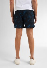 Czarne kąpielówki w niebieskie kwiatowe wzory z teksturowanym wykończeniem. Posiadają tylną kieszeń i luźny krój. Nosi się je z białymi trampkami.