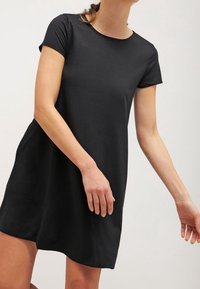 Svart kortärmad klänning med rund halsringning, tillverkad av lätt material. Lätt lös passform med en slät textur och knälång nederkant.