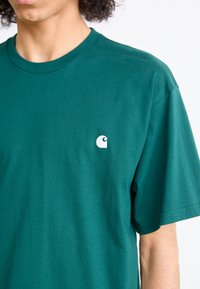 Green cotton t-shirt featuring a crew neck and short sleeves. A small white logo is positioned on the upper left chest area.