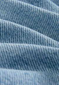 Detailný záber svetlomodrej rifľoviny zobrazujúci diagonálnu tkaninu a jemné záhyby.