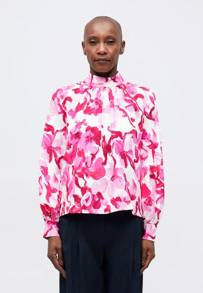 Blouse florale avec un col haut, présentée sur une base blanche avec des motifs abstraits roses. Manches longues avec des poignets froncés, coupe décontractée.