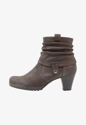 Brown suede ankle boot with a folded cuff, decorative strap and silver snap accent, and a tapered heel. Textured surface and low-profile sole.