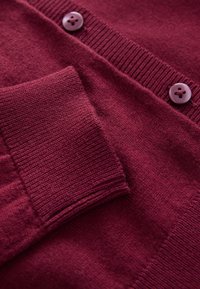 Bordeaux gebreid vest met een geribbelde kraag, een gladde textuur, twee knopen en een voorkantzak met een subtiel getextureerde afwerking.