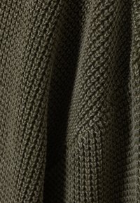 Dark green knitted fabric featuring a textured pattern with raised stitches and varied thickness, creating a soft, tactile appearance.
