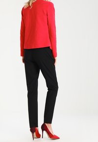 Red textured blazer, black tapered pants, and two-tone red high heels. The blazer features a clean cut with a round neckline.