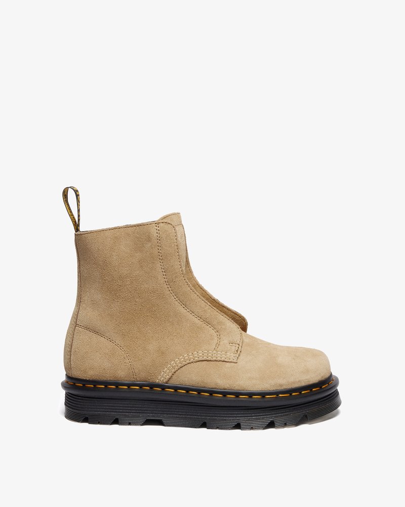 Botine scurte din suede bej, cu o textură netedă, panouri laterale elastice, tab de prindere și talpă neagră cu cusături galbene și profil antiderapant.