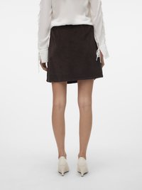 Jupe en velours côtelé marron avec une silhouette évasée et une texture lisse, associée à un blouse blanche et des chaussures à talons légers.