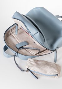 Lichtblauwe leren rugzak met een ritssluiting, voorzien van een gestreepte beige binnenkant, een klein vakje en meerdere organisatiecompartimenten.