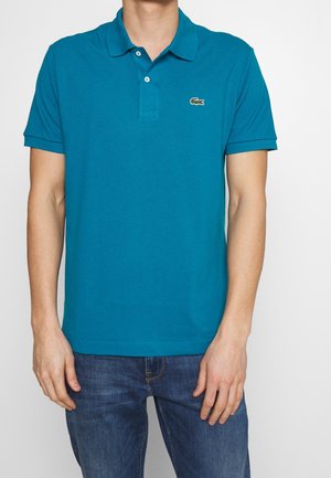 Turkusowa koszulka polo wykonana z bawełny, z kołnierzykiem i trzema guzikami. Małe logo na lewej piersi. Noszona z niebieskimi dżinsami.